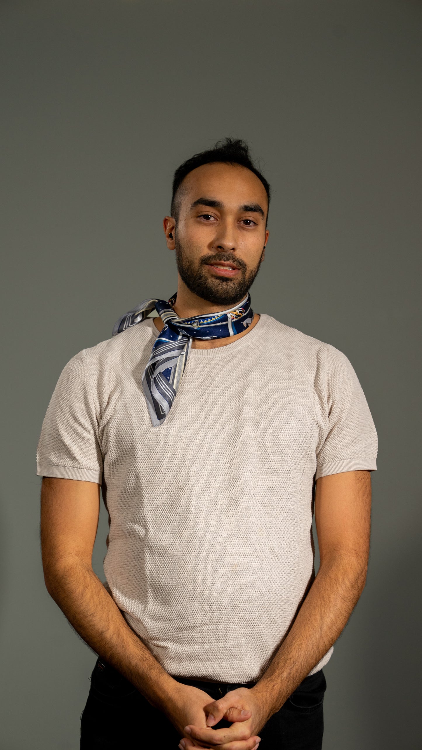 male model wearing colourful square silk scarf, 100% pure silk, design with horses and predominantly blue and white/beige tones, loosely wrapped around the neck. Front angle
