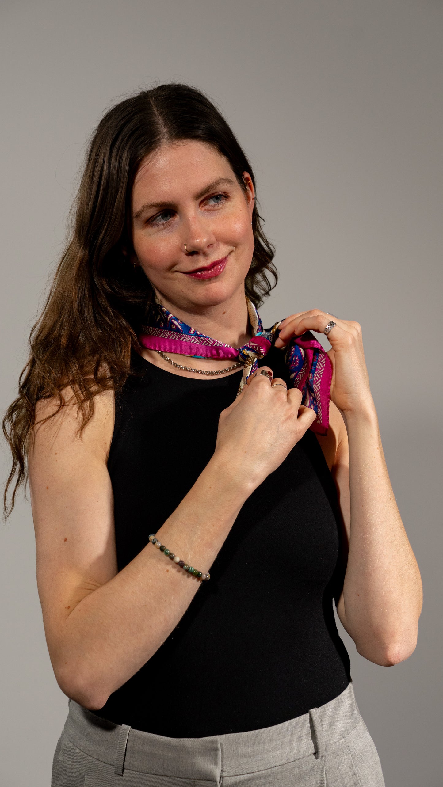 female model wearing a square handwoven 100% pure silk scarf with vibrant blue, purple, and pink colours and intricate designs, and looking to the side smiling