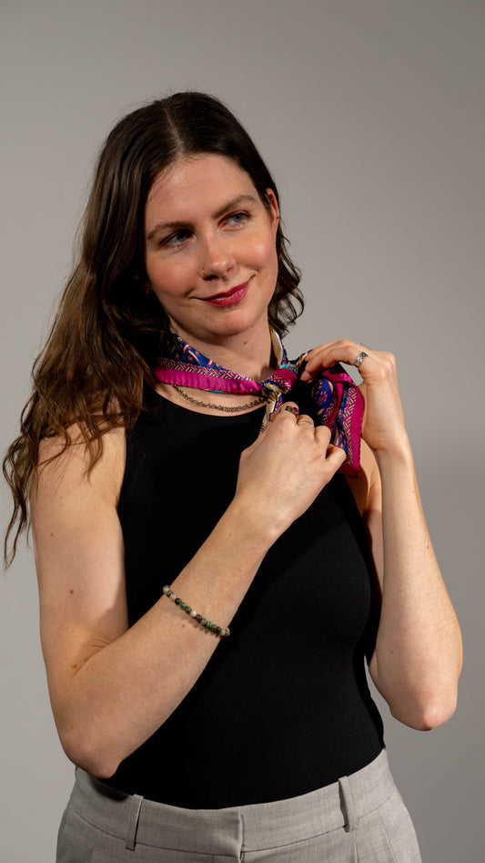 female model wearing a square handwoven 100% pure silk scarf with vibrant blue, purple, and pink colours and intricate designs, and looking to the side smiling