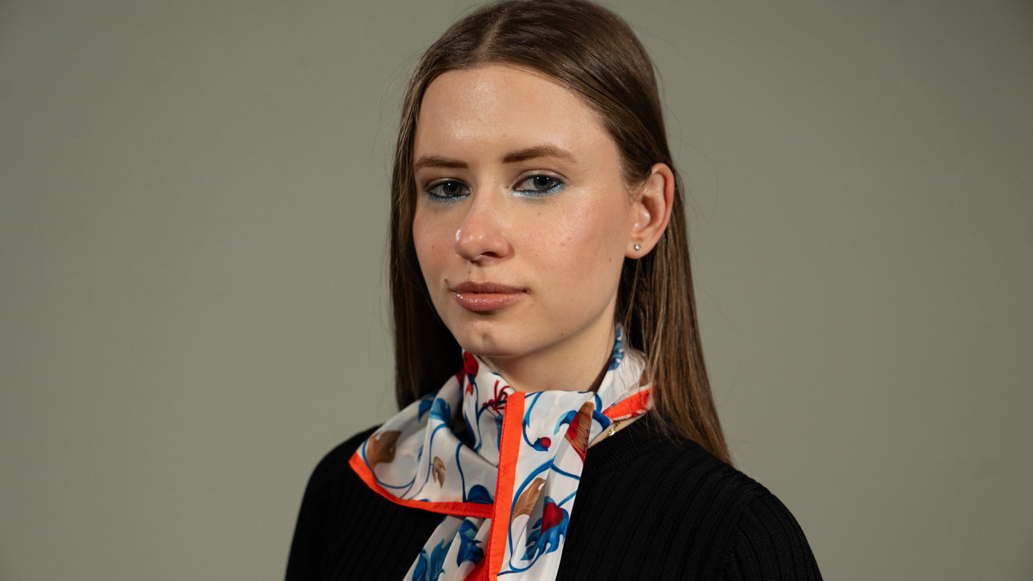 a female model wearing a colourful square vegan silk bandana including blue, white, red, and brown, featuring birds as a neck scarf