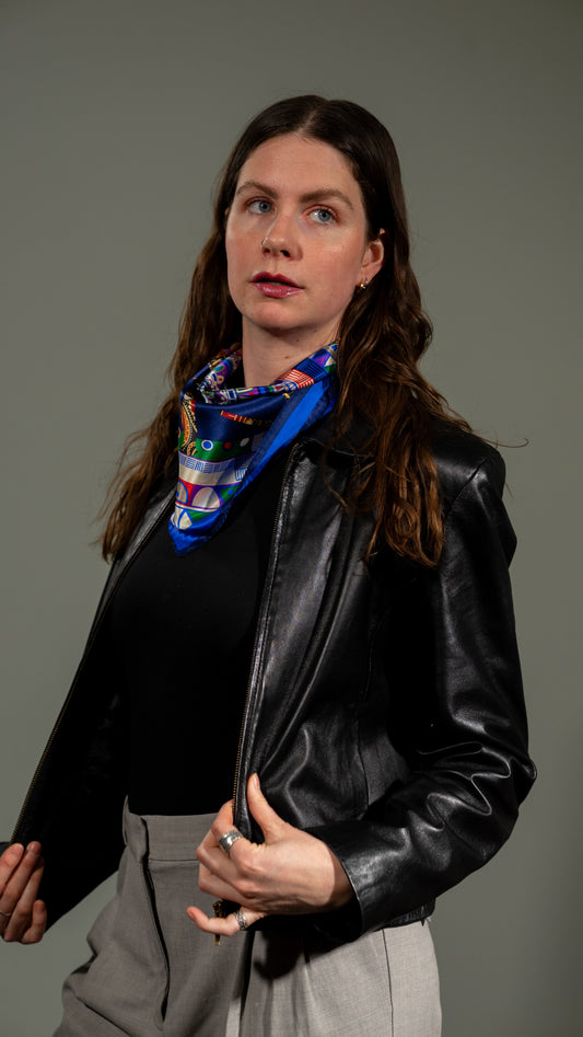 female model in a black leather jacket wearing a colourful square silk scarf, 100% pure silk with mandala design and predominantly blue tones, looking off camera