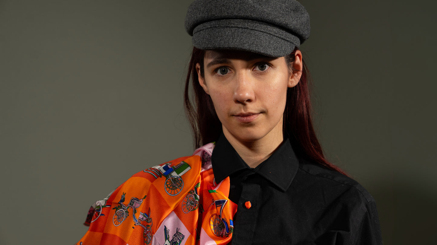 close-up of model wearing a colourful square silk scarf, 100% pure silk, design with victorian vehicles and predominantly orange tones, front facing.