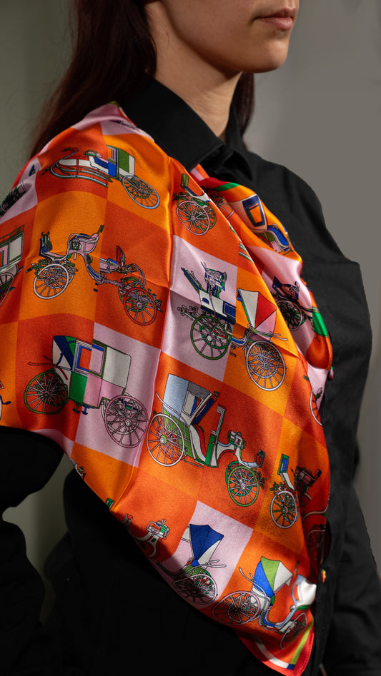 model wearing a colourful square silk scarf, 100% pure silk, design with victorian vehicles and predominantly orange tones, styled over the shoulder