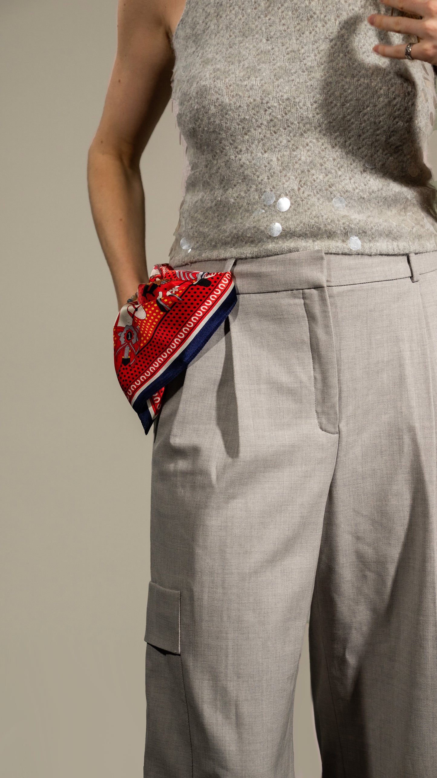 model wearing a square silk scarf, 100% pure silk, design with humans and race horses, predominantly red and white tones. Styled to attach to the belt line.
