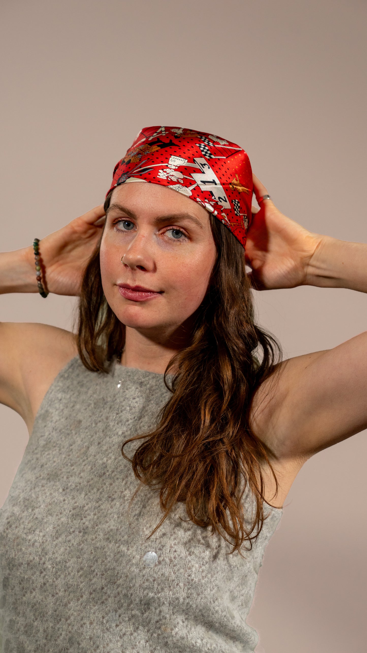female model wearing a square silk scarf, 100% pure silk, design with humans and race horses, predominantly red and white tones, styled as a hair wrap.