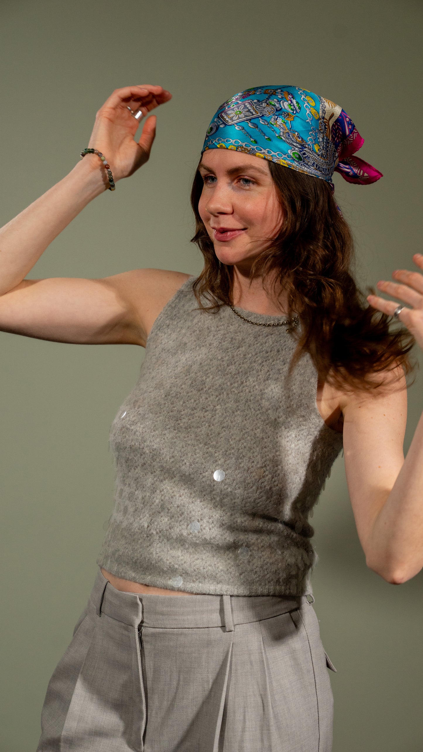 a female model wearing a square handwoven 100% pure silk scarf with vibrant blue, purple, and pink colours and intricate designs as a hair wrap, looking off-camera.