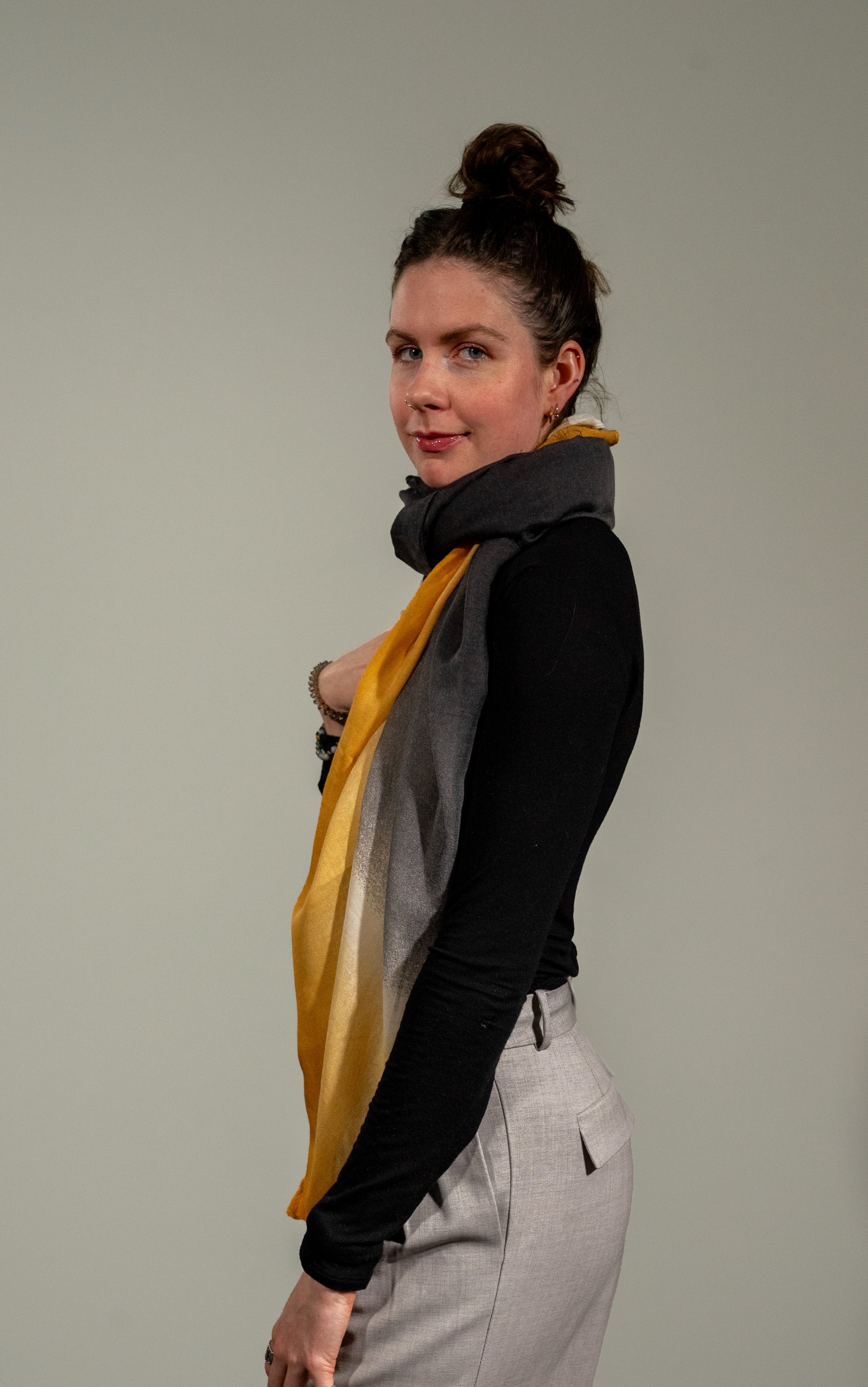 model full size shot from side, looking at camera and wearing wool silk shawl with light pink/orange, yellow, white, and black.