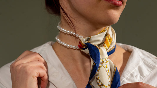 close-up of a model wearing an elegant square handwoven 100% pure silk scarf with beige, gold, and blue colours as a neck wrap, tied with her jewelry.