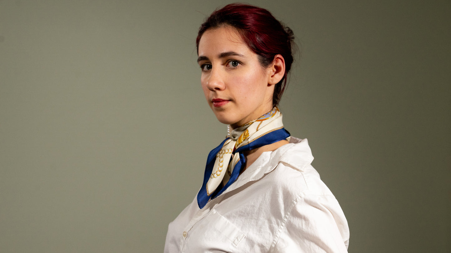 a female model wearing an elegant square handwoven 100% pure silk scarf with beige, gold, and blue colours, looking at the camera.