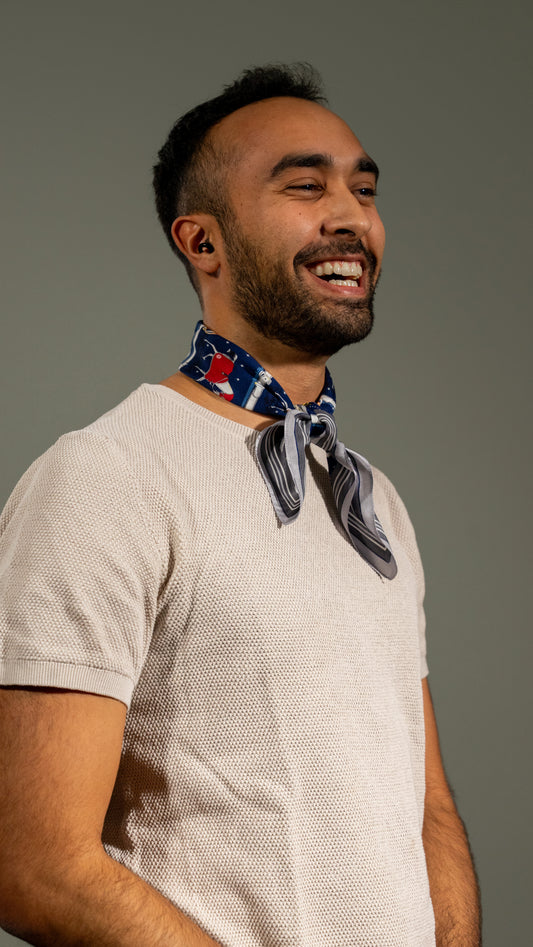 male model laughing and wearing colourful square silk scarf, 100% pure silk, design with horses and predominantly blue and white/beige tones, loosely wrapped around the neck