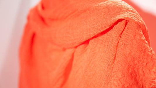 a soft, orange, handwoven wool silk scarf, hanging.