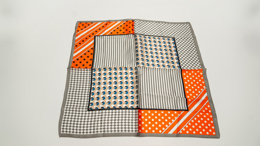 a square 100% pure silk scarf with a colourful geometric designs, featuring orange, white, and grey.